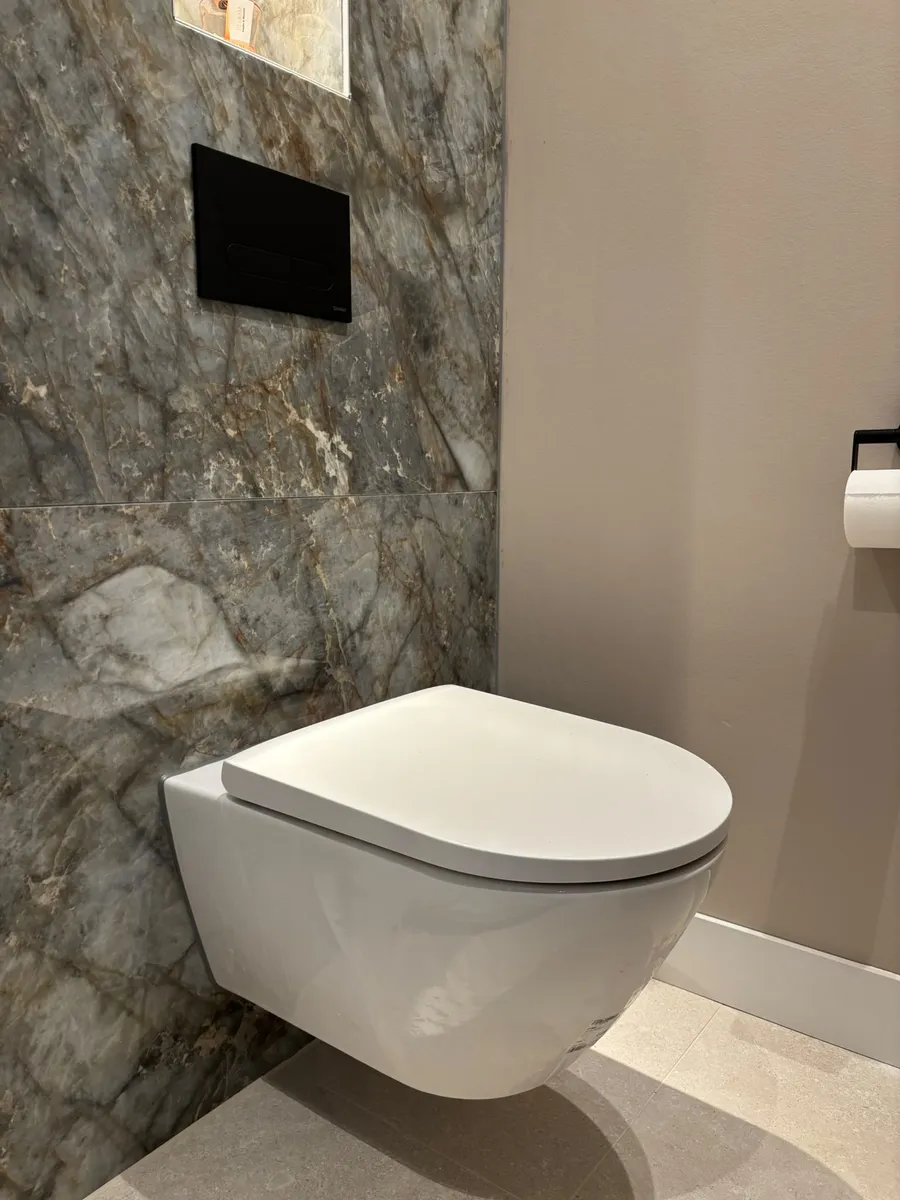 Strakke zwarte drukplaat op een marmeren toiletwand, een heel ander model dan de witte tweeknops-plaat