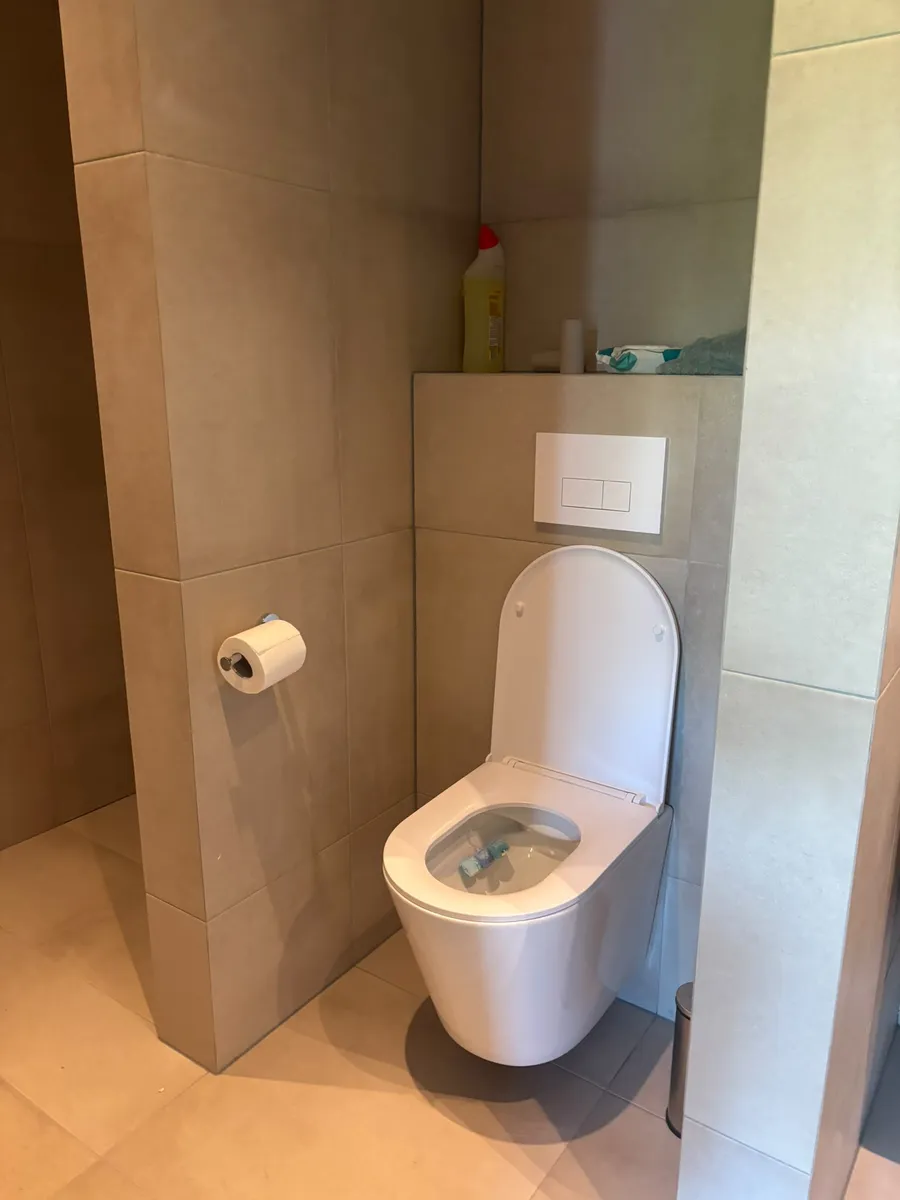 Strak afgewerkt hangtoilet met witte tweeknops-drukplaat, geplaatst door een loodgieter in Helmond