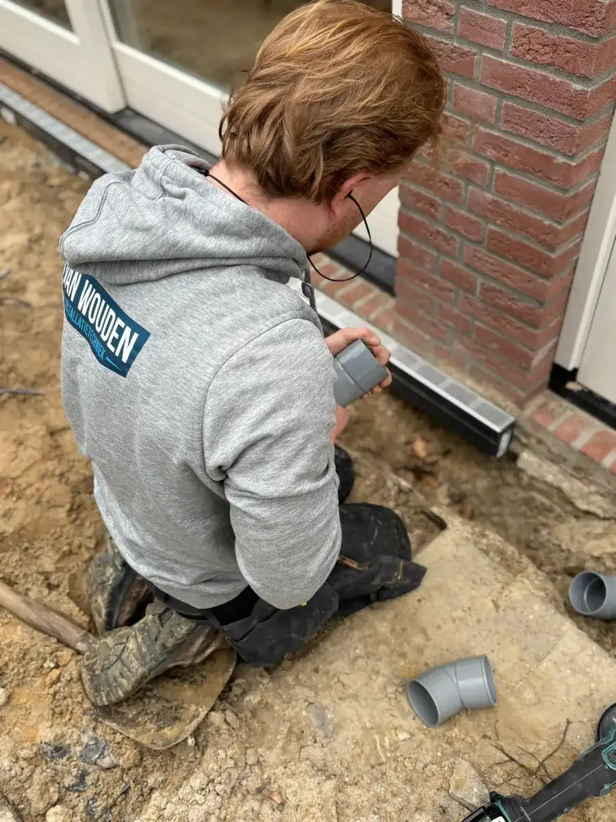 Phil van Wouden monteert nauwkeurig een afvoerleiding, met waterpas, bij een woning in Helmond