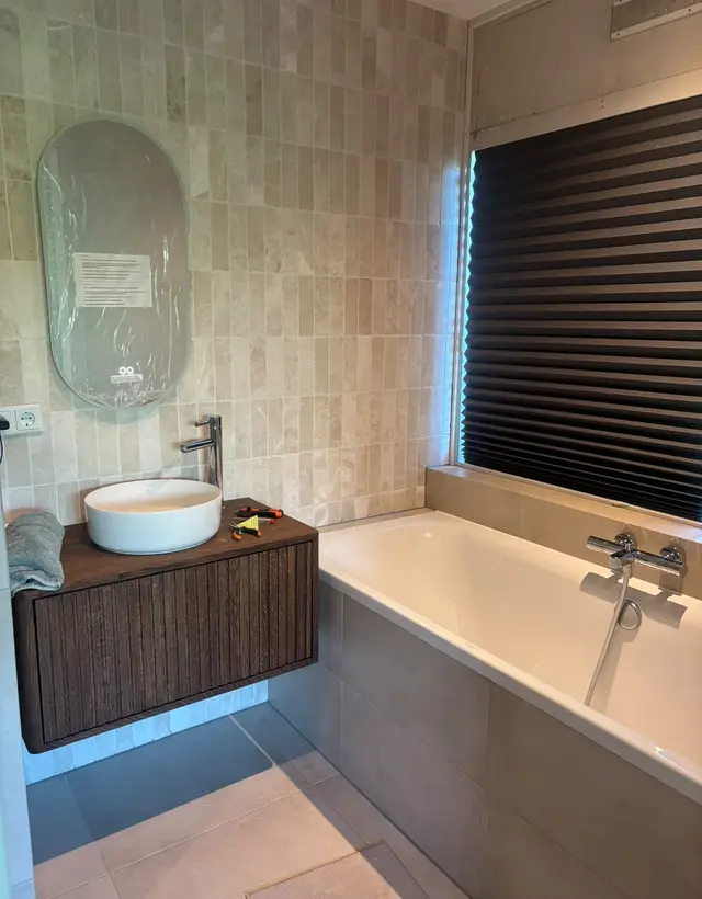 Badkamer met ligbad, badmengkraan en zwevende wastafel op een houten meubel, geïnstalleerd in Helmond