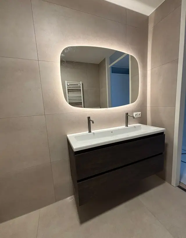 Dubbele wastafel met twee kranen en een verlichte spiegel, aangesloten in een nieuwe badkamer