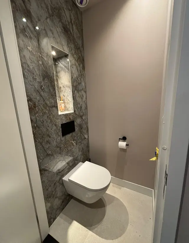 Toilet met marmeren wand, verlichte nis en zwarte drukplaat, compleet geïnstalleerd