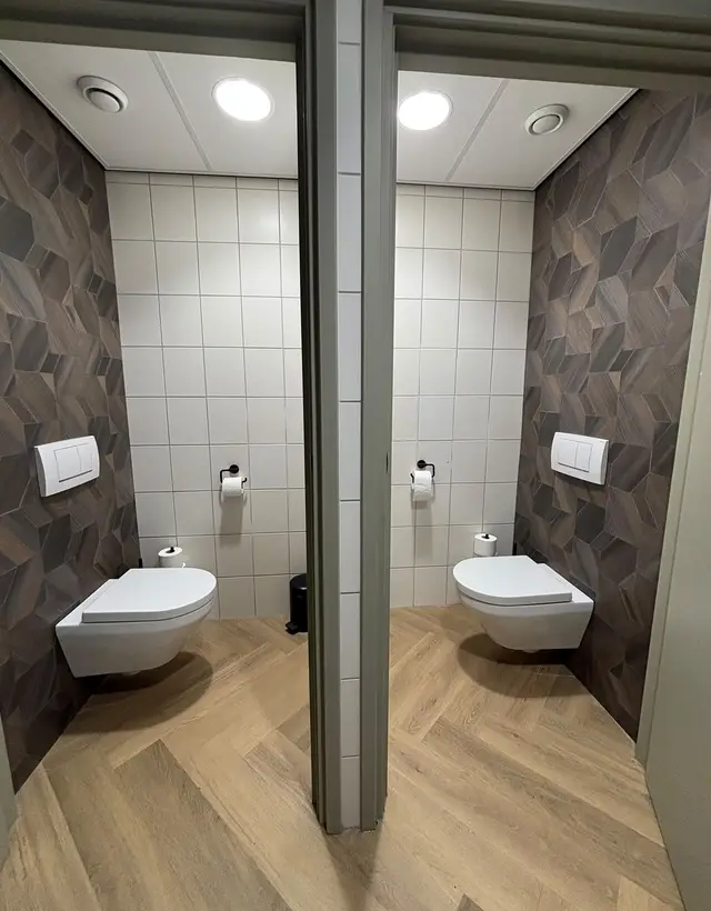 Twee hangtoiletten met drukplaten in een zakelijk sanitairblok, door Van Wouden geïnstalleerd